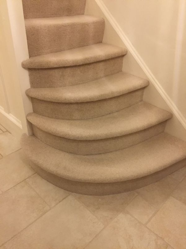 Pale carpet fitted down curved stairs to a stone-tiled hall in Minchinhampton
