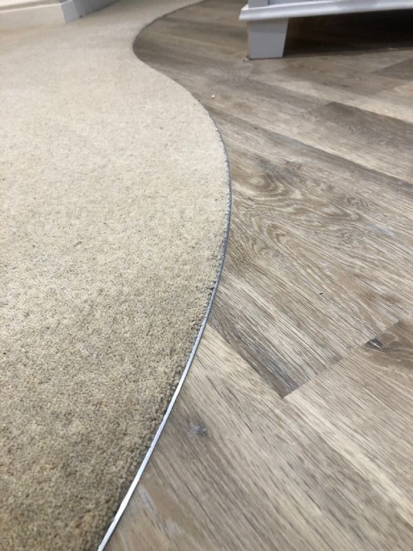 Curved threshold cut between carpet and grey oak-effect plank flooring